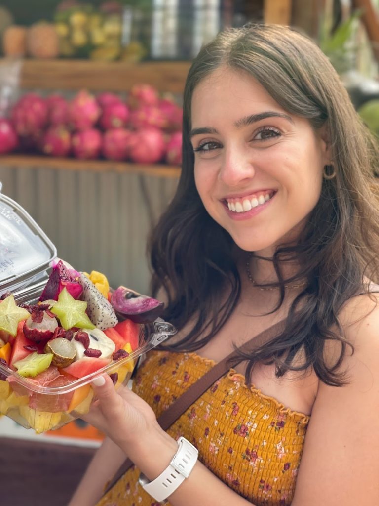 Faith smiling to the camera while holding fresh fruit from a farmers marketing